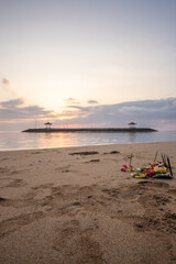 Fototapeta na wymiar Sunrise at the sandy beach of Sanur. Temple in the water. Offerings by the sea on the beach. Hindu faith in Sanur on Bali. Dream island and dream destination