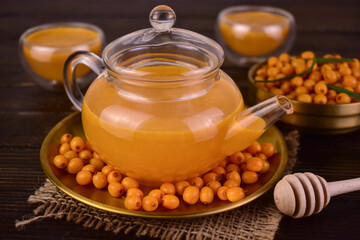 Vitamin tea from sea buckthorn in a glass teapot on a dark background.
