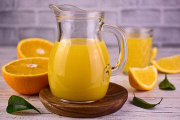 Orange juice in a glass decanter and fresh oranges.