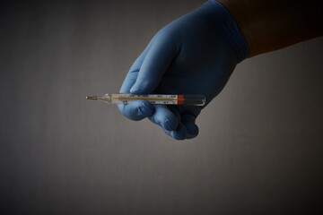 A hand in a blue medical glove holds a mercury thermometer. Diagnosing and treating diseases and...