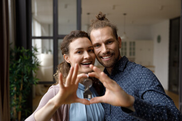Happy dating millennial man and woman in love showing hand heart shape, joining fingers, looking at camera, smiling, laughing. Romantic couple home head shot portrait. Valentines day concept