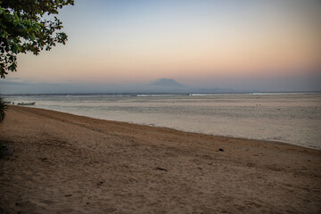 Beautiful sunrise on Sanur beach. Temple in the calm sea. Small waves in the morning. Sandy beach on the dream island of Bali. in the background the volcano Mount Agung