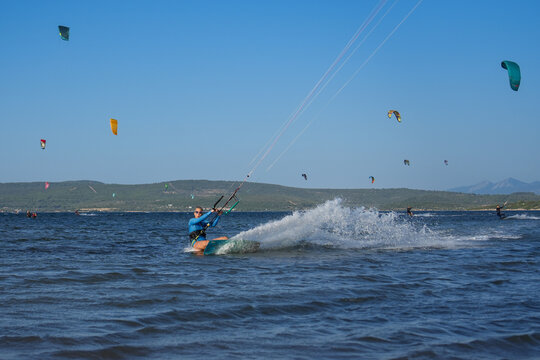 Beautiful girl  with blond hair kitesurfing in blue sea splashing water with kites in the background