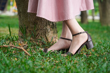 Close up of woman feet in summer. sandals shoes. high heels. with fresh green grass. beside the tree
