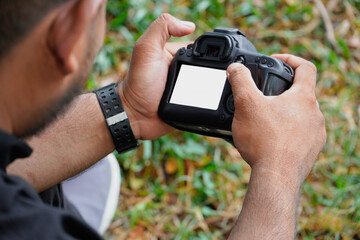 Man holding and looking at camera to check his shot. digital camera in man hand. nature background