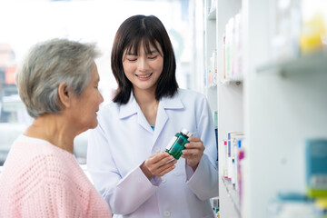 Fototapeta premium Young Asian pharmacist talking with customer at pharmacy counter. She tells customers about drug information at the pharmacy.