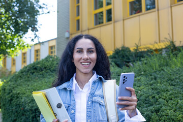 Portrait of cheerful woman looking at the camera hand holding a phone and folders with papers....