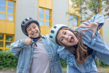 Two school-age children, a boy and a girl in helmets, in the school yard against the backdrop of...