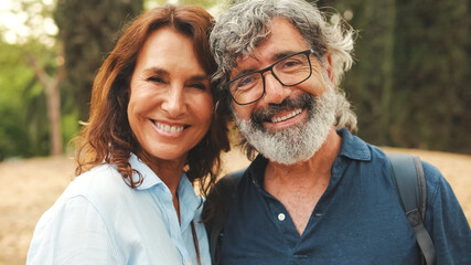 Fototapeta premium Close up, smiling older married couple looking at the camera while standing in the park hugging each other