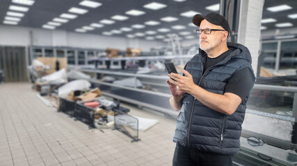 Man inside supermarket under construction. Guy with phone is typing SMS. Supermarket worker...