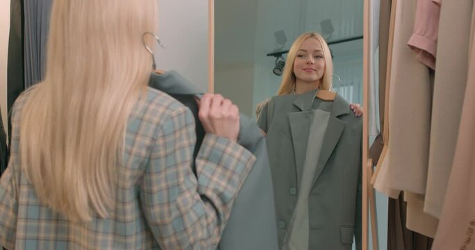 A young elegant woman is going to a meeting, chooses clothes in front of a mirror. Hard choice routine of what clothes to wear. Getting dressed. stylist matching clothes in shop beauty, shopping Sale