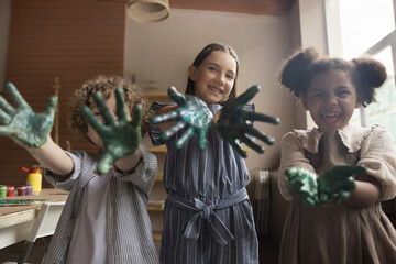 Happy kids showing painted palms smiling looking at camera. Playful three multiethnic little...