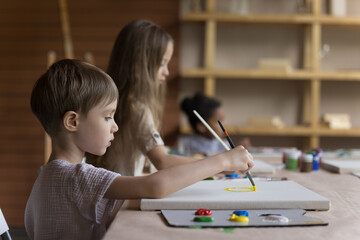 Beautiful kids painting pictures on canvas sit at table in art-studio. Group classes of art for...