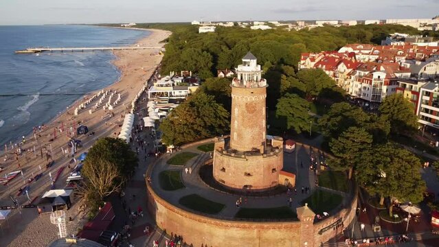 A lighthouse at sunset on the Baltic Sea. A sandy beach in Kolobřeh. A drone that rotates around a lighthouse. Kołobrzeg is city in Poland. 4k video
