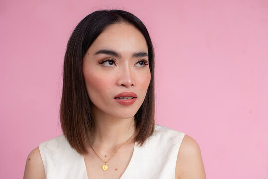 A typical asian woman with medium length hair wearing a cream sleeveless blouse. Against a pink background.