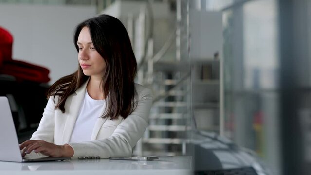 Business woman working on a laptop and using phone at the office of car showroom 