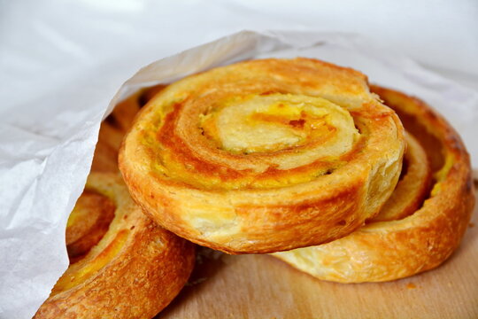 fresh ruddy hot breakfast baking pastries with a crispy crust and sweet filling from the bakery in white paper on wooden table close up