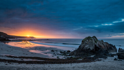 Beautiful sunrise landscape image of Kennack Sands in Cornwall UK wuth dramatic moody clouds and vibrant sunburst