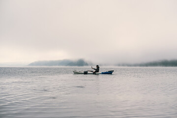 Woman kayaking on a mountain lake. Clouds and fog above the water