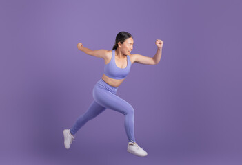 Fototapeta na wymiar Young asian woman in sportswear running over purple studio background, free space