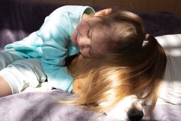 little cute girl hugs a beagle dog sitting on the bed
