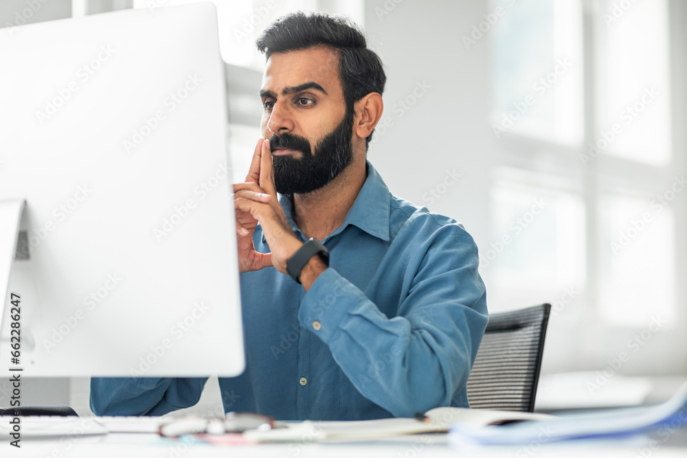 Poster focused indian middle aged businessman sitting at worktable in front of computer at office