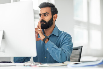 Focused indian middle aged businessman sitting at worktable in front of computer at office