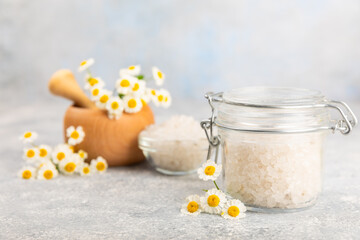 Fototapeta na wymiar Spa sea salt on texture background. Sea salt with chamomile extract in a glass jar on the table. Beauty concept. Sea bath salt. Place for text, copy space.Close-up.