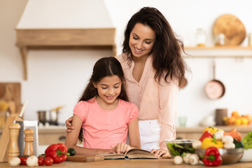 Mom and kid daughter looking through recipe book in kitchen