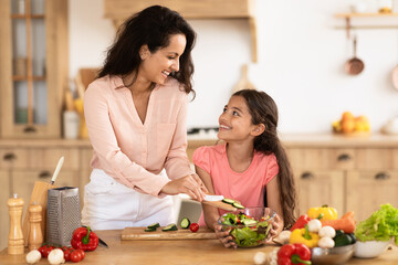Happy mother and little daughter cooking vegetable salad together indoor