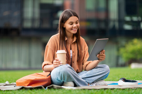 Relaxed young woman student drinking coffee, using digital tablet