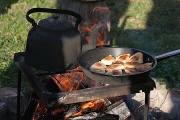 An old metal kettle and pan with dumplings stands by campfire