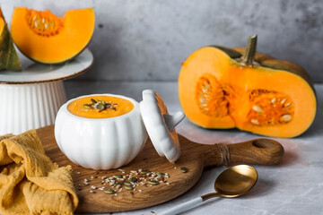 Seasonal autumn food. Traditional pumpkin cream soup in a pumpkin-shaped bowl and fresh pumpkin on a gray marble background.