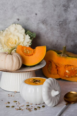Seasonal autumn food. Traditional pumpkin cream soup in a pumpkin-shaped bowl and fresh pumpkin on a gray marble background.