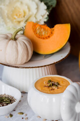 Seasonal autumn food. Traditional pumpkin cream soup in a pumpkin-shaped bowl and fresh pumpkin on a gray marble background.