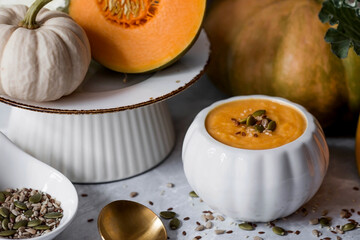 Seasonal autumn food. Traditional pumpkin cream soup in a pumpkin-shaped bowl and fresh pumpkin on a gray marble background.