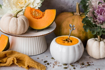 Seasonal autumn food. Traditional pumpkin cream soup in a pumpkin-shaped bowl and fresh pumpkin on a gray marble background.