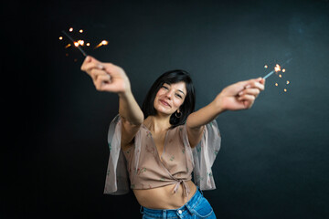 Happy beautiful woman holding festive sparkler among Christmas night