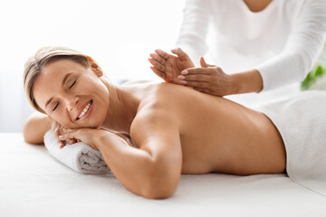 Obraz premium Beautiful middle aged woman relaxing on massage table while masseur hands providing therapeutic back session in luxury spa salon