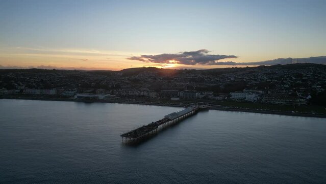 Paignton, Torbay, South Devon, England: DRONE VIEWS: Paignton Pier at sunset. Paignton is a popular UK holiday resort; the Pier was completed in 1879 during the reign of Queen Victoria (Clip 6).
