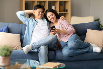 Happy Japanese spouses browsing internet at cozy home