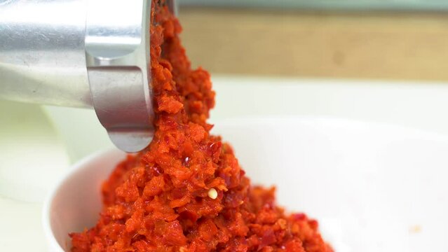 Grinding red pepper in a meat grinder. The resulting product exits through the holes. Close-up. Side view.
