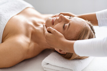 Obraz na płótnie Canvas Beautiful middle aged woman enjoying rejuvenating face lifting massage at spa salon
