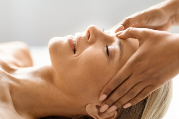 Beautiful middle aged woman immersing in soothing acupressure head massage at spa