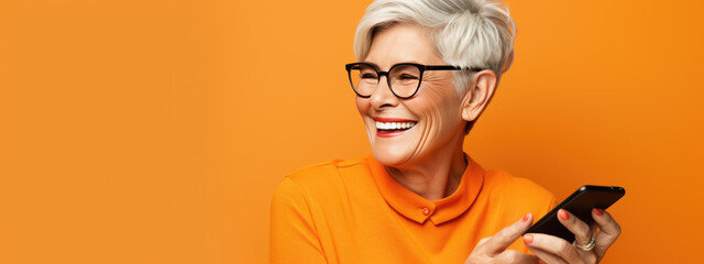 An elderly woman smiling and laughing with her phone against a colored background. - obrazy, fototapety, plakaty
