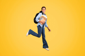 Fototapeta na wymiar Cheerful teen european lady with backpack, headphones and books jump, freeze in air