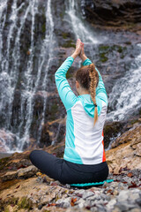 Meditation in nature, a girl relaxing in an easy yoga pose near a scenic waterfall. Serene, vitality, and harmony concepts.