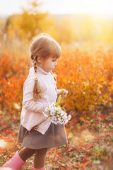 Little 4-old adorable baby girl with flowers playing in the sunny autumn park
