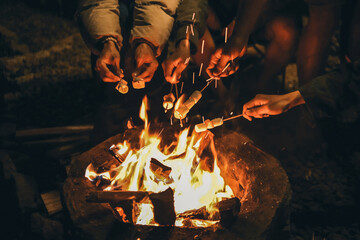 Hands of friends roasting marshmallows on the fire at campsite - obrazy, fototapety, plakaty