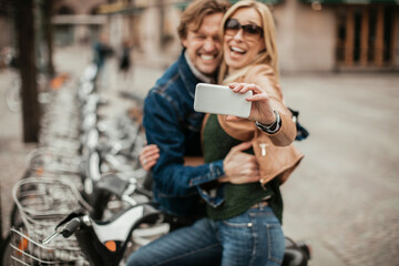 Middle aged Caucasian couple taking a selfie on a smartphone at the bike sharing program in the city